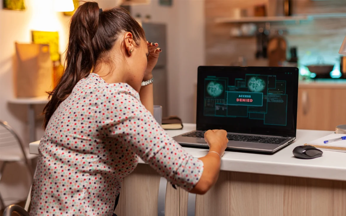 Mujer preocupada frente a laptop con mensaje de acceso denegado por ciberataque